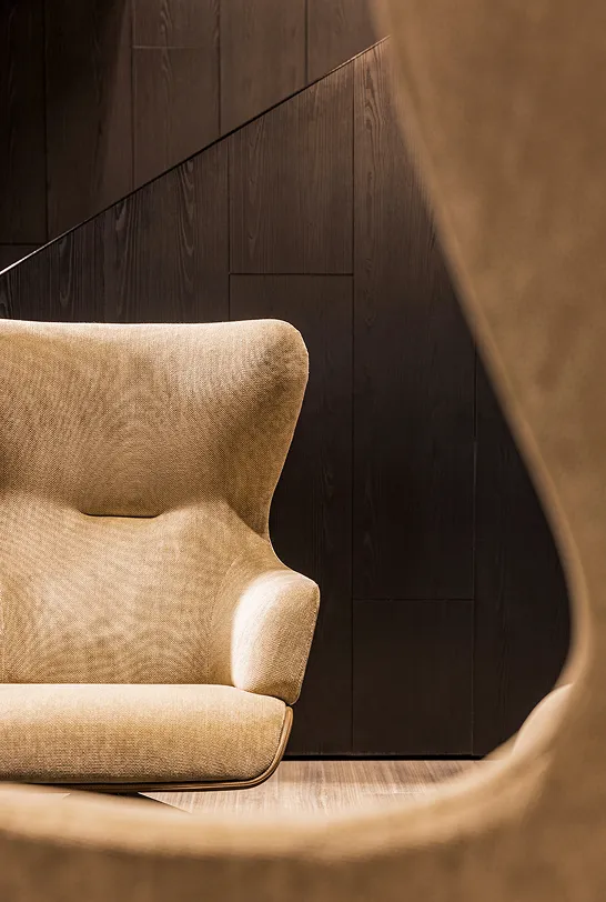 Poltrona beige dal design moderno con schienale alto davanti a parete di legno scuro.