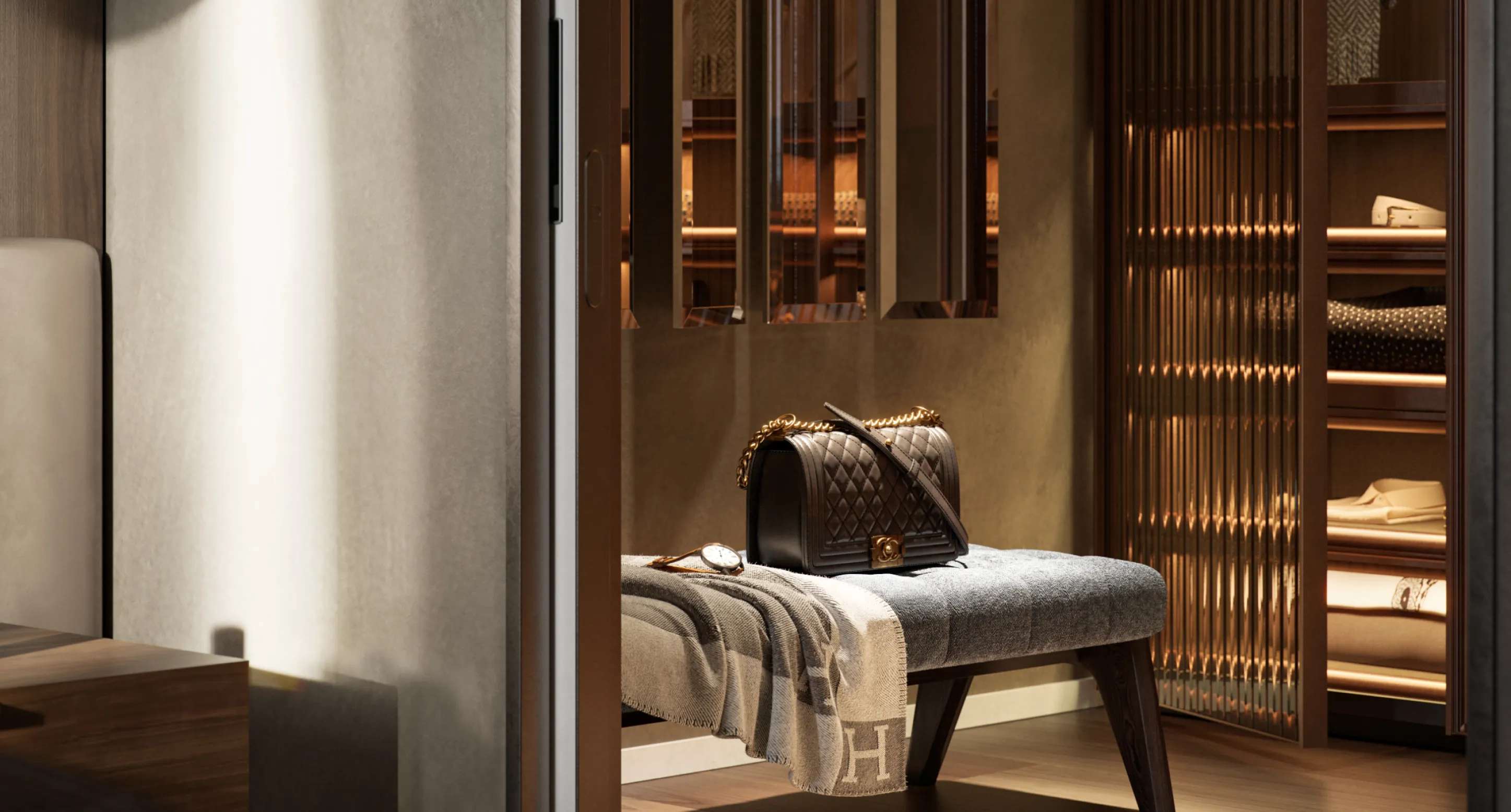 Borsa nera con catena dorata appoggiata su una panca grigia con coperta beige e orologio, in una stanza elegante con armadio in legno e vetro.