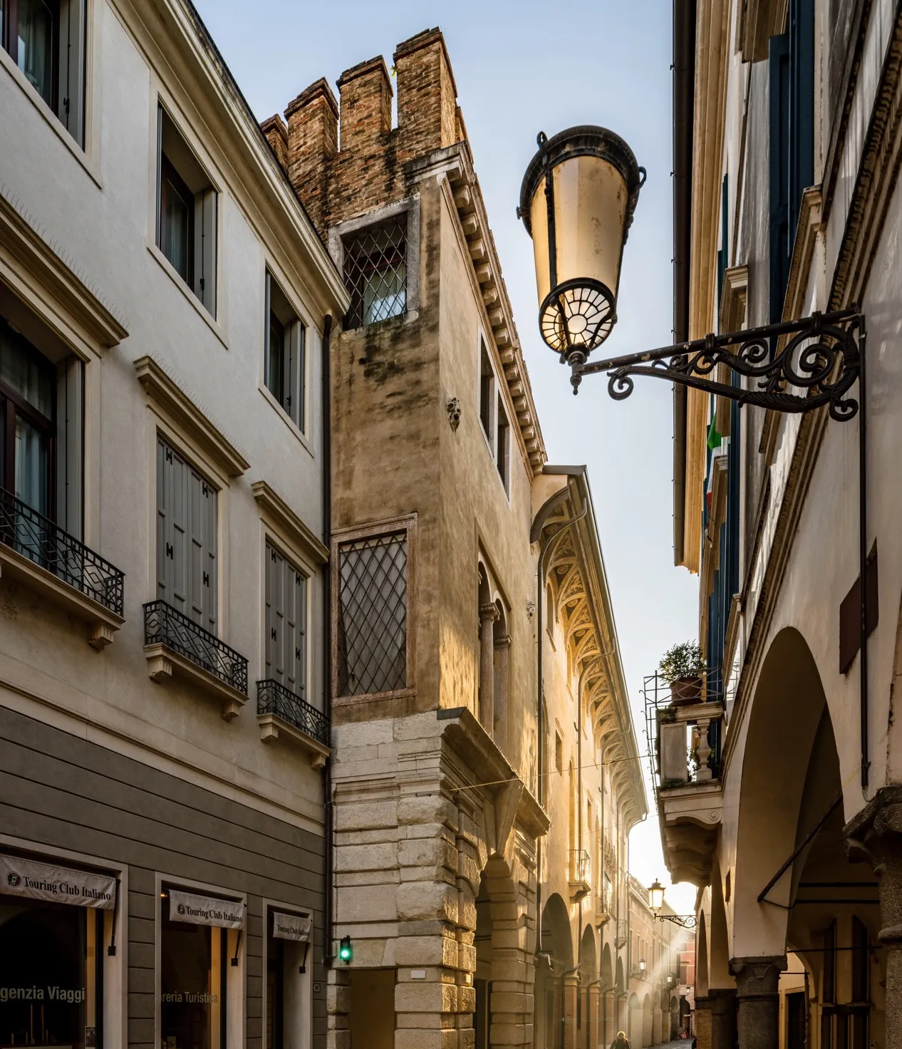 Stretta via cittadina con edifici storici in pietra, finestre decorate e lanterna vintage, illuminata dalla luce del sole al tramonto.