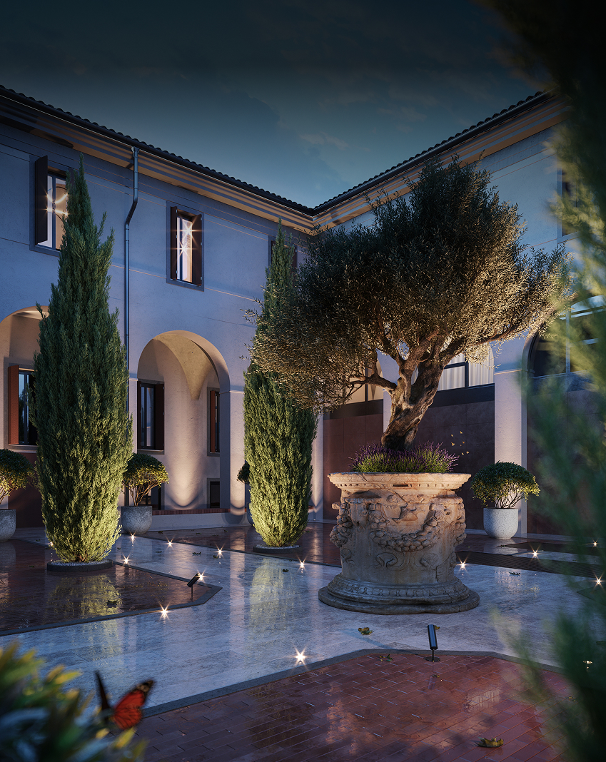 Elegant courtyard with illuminated tall trees and a large ornate stone planter holding a blooming tree at dusk.