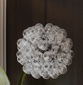 Modern spherical chandelier made of clustered clear glass bulbs hanging indoors against a dark wood background.